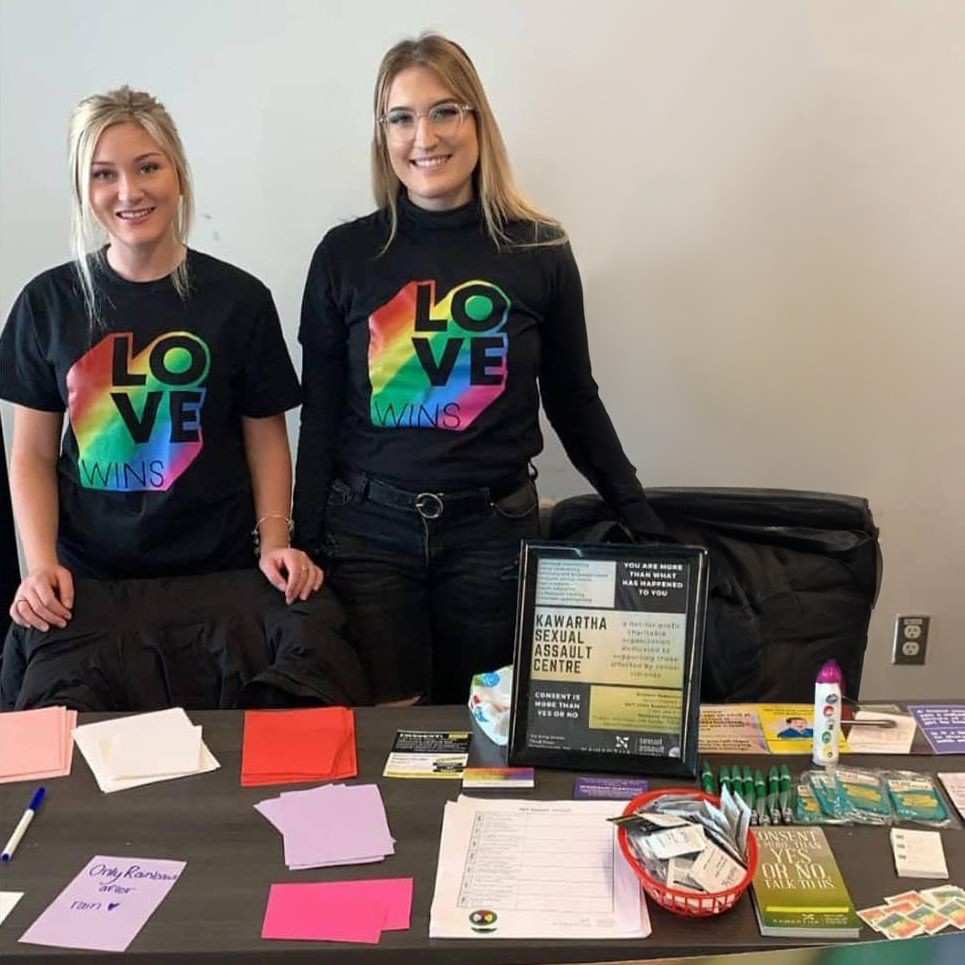 Staff at a KSAC booth share resources wearing t-shirts with the words "love wins" in rainbow motif