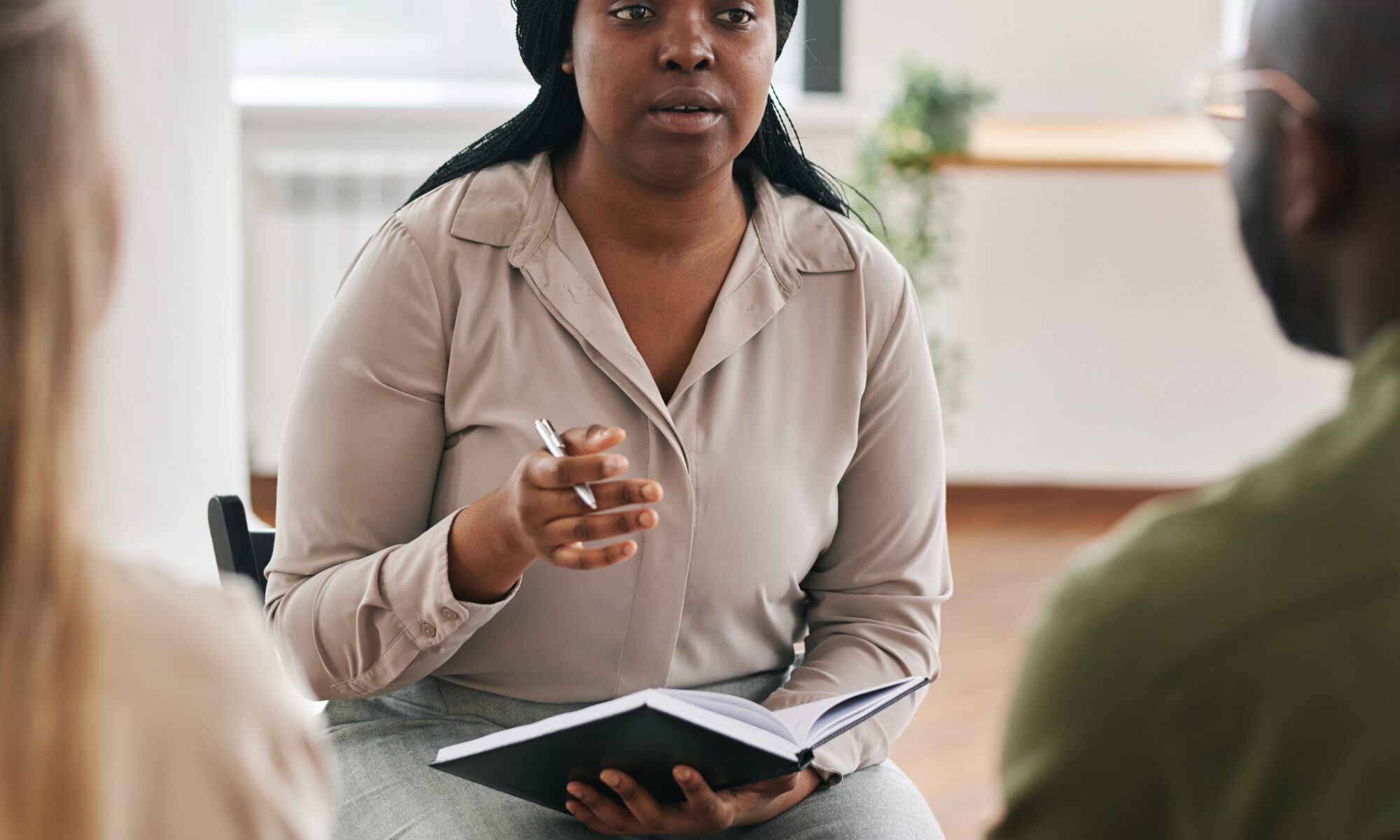 Young confident black woman with notebook and pen consulting intercultural couple sitting in front of her.